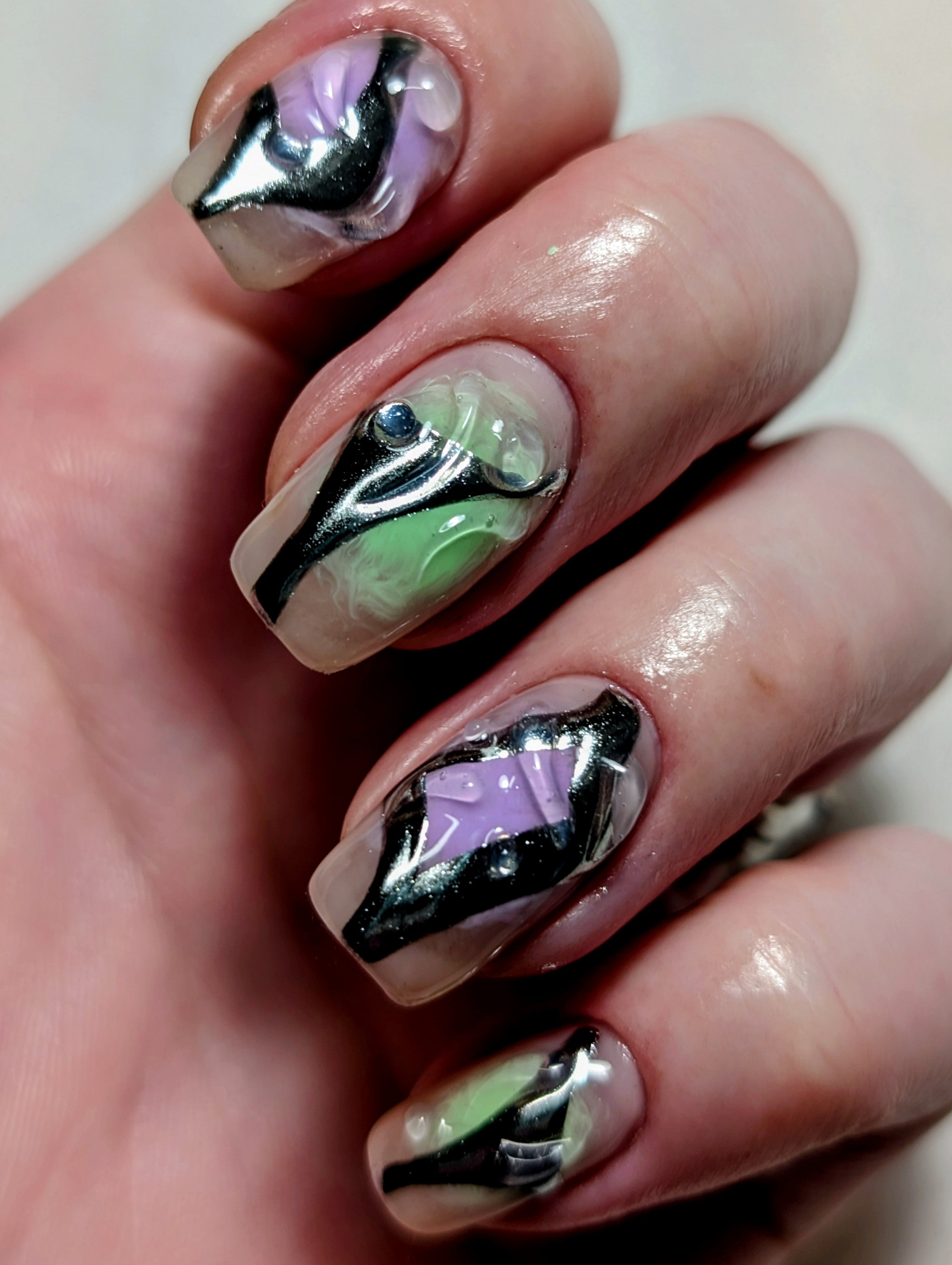 Close-up of a hand with decorative nail art featuring metallic and pastel colors.